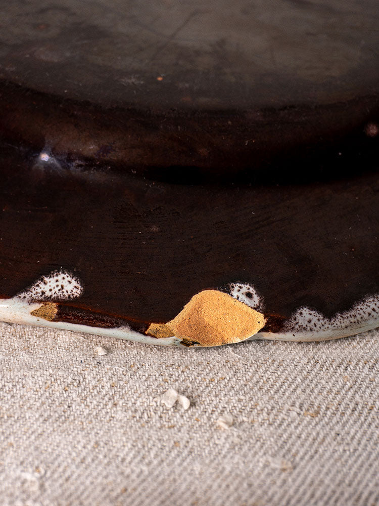 Antique French faience plate with Cul Noir design, 19th century, chipped edge gold-repaired, on textured beige fabric.