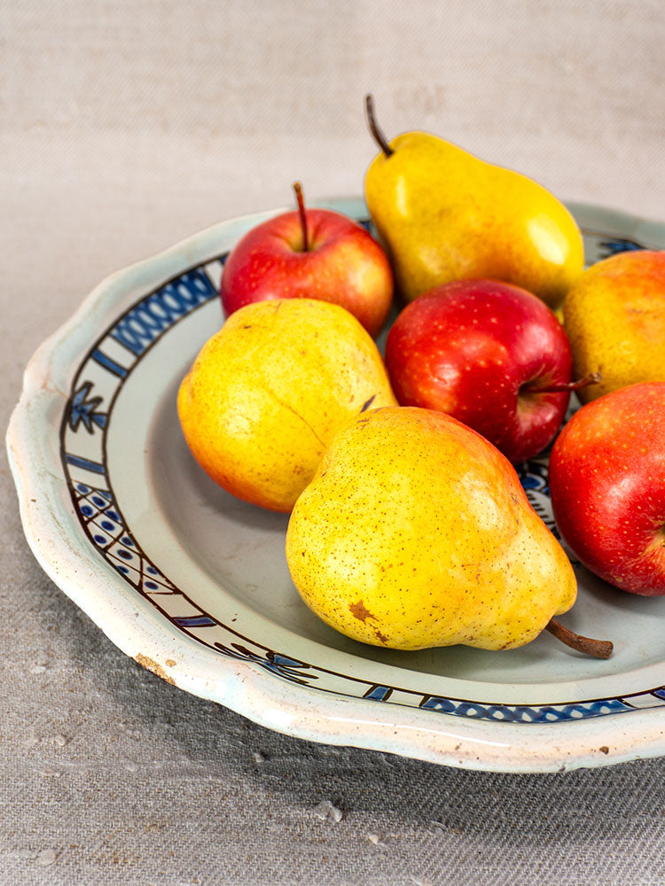 19th-century French faience plate with three yellow pears and four red apples on beige fabric.