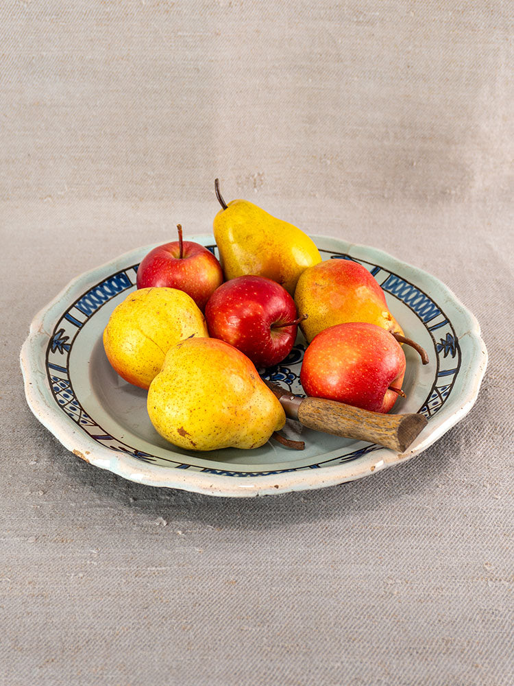 Antique 19th-century French faience Cul Noir plate with blue designs, styled with pears and apples on beige fabric.