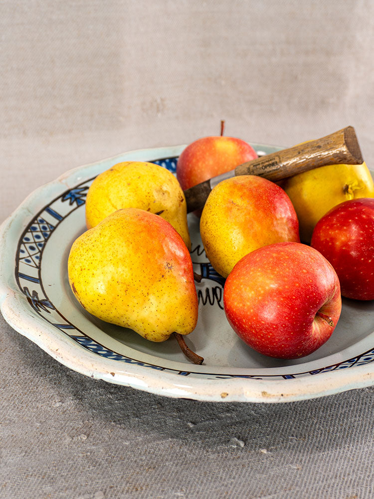Antique French faience plate with classic blue patterns, styled with pears, apples, and a wooden-handled tool.
