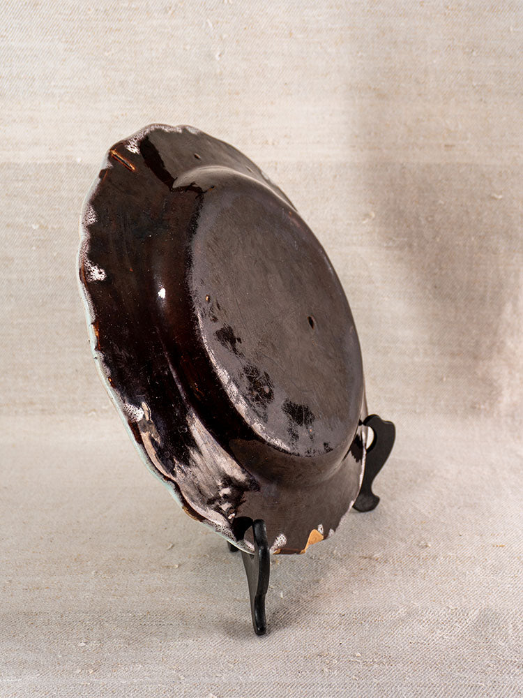 19th-century French faience plate with wavy edge, back view on stand; visible rim chips.