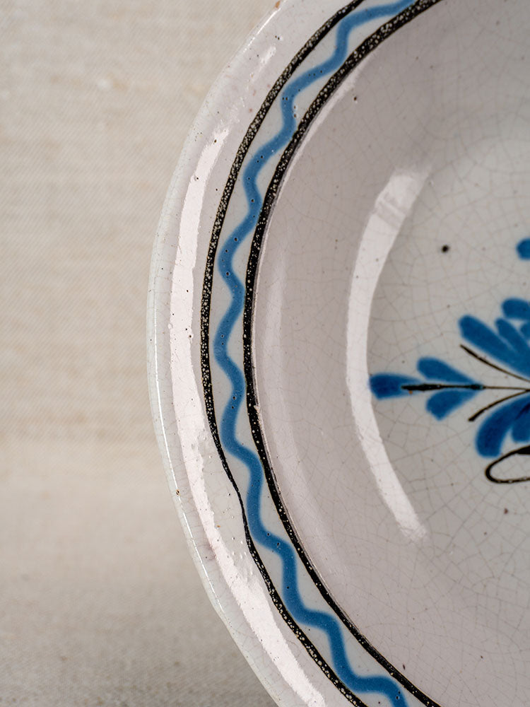 Detail of antique French Cul Noir faience charger with blue wavy line, black rim, crackled glaze, Panier Fleuri floral motif.