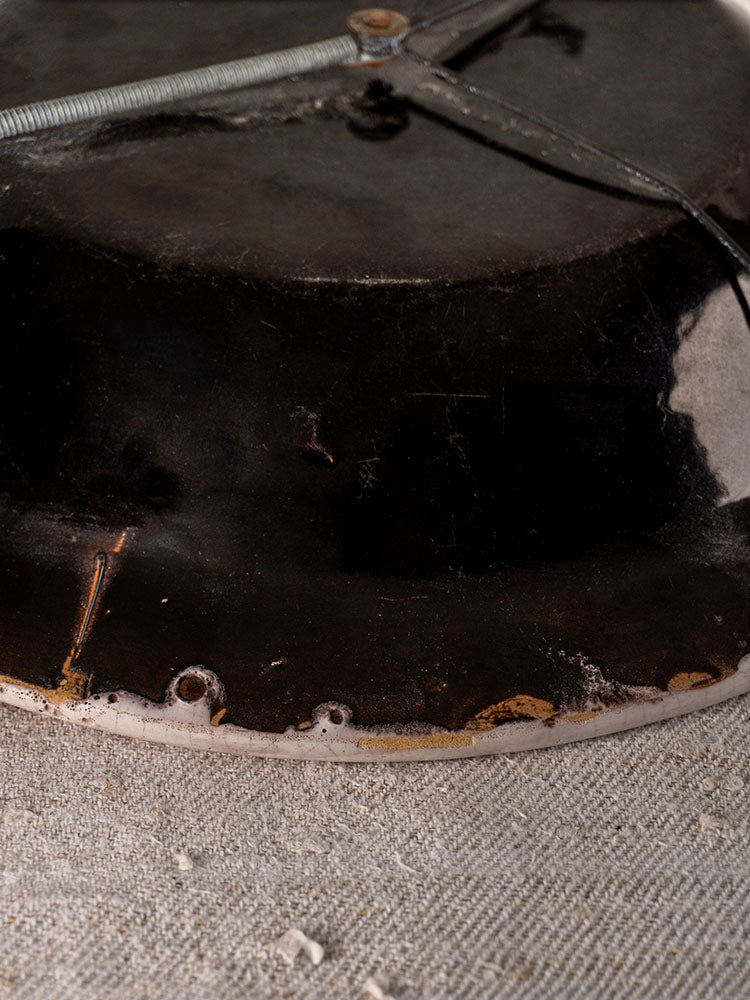 Antique French Cul Noir faience charger underside with worn dark glaze, rust spots, wire, on textured fabric surface.