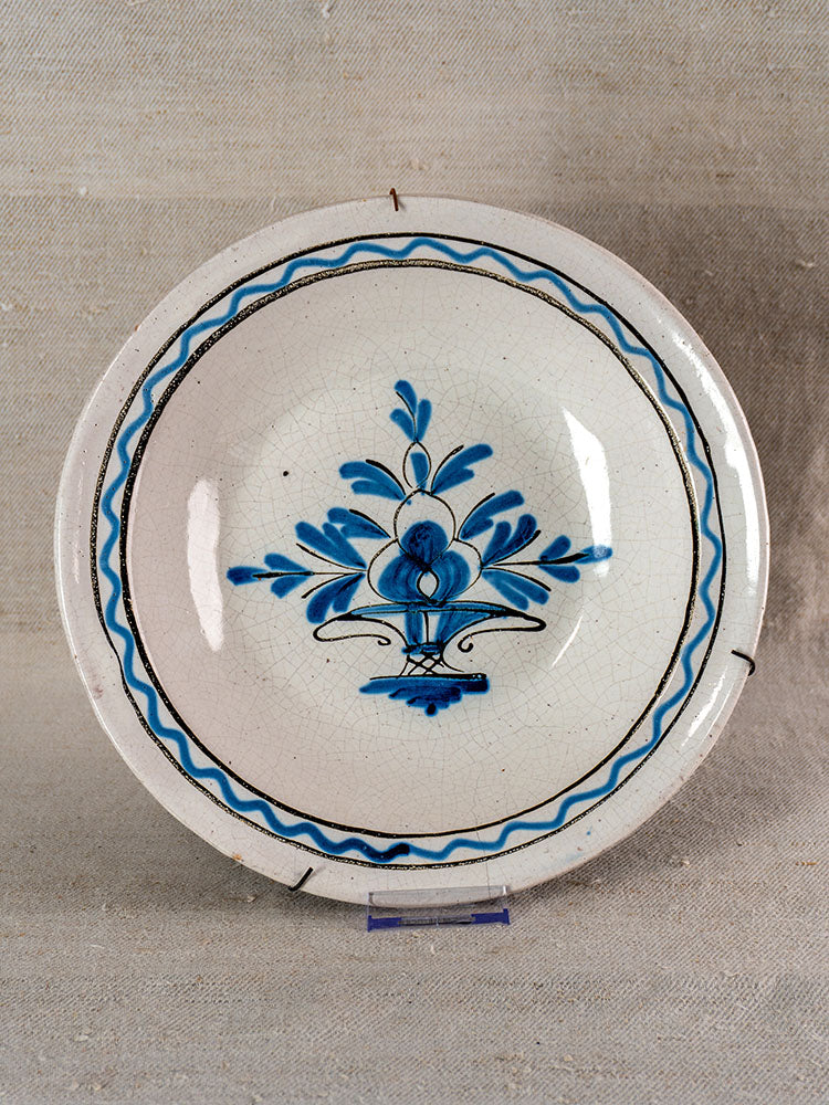 Antique French Cul Noir faience charger, late 18th century, blue Panier Fleuri motif, cracks, metal repairs; neutral fabric backdrop.