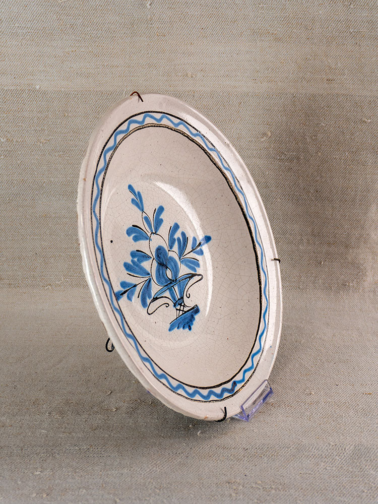 Antique French Cul Noir faience charger with hand painted blue floral motif and wavy border on a display stand.