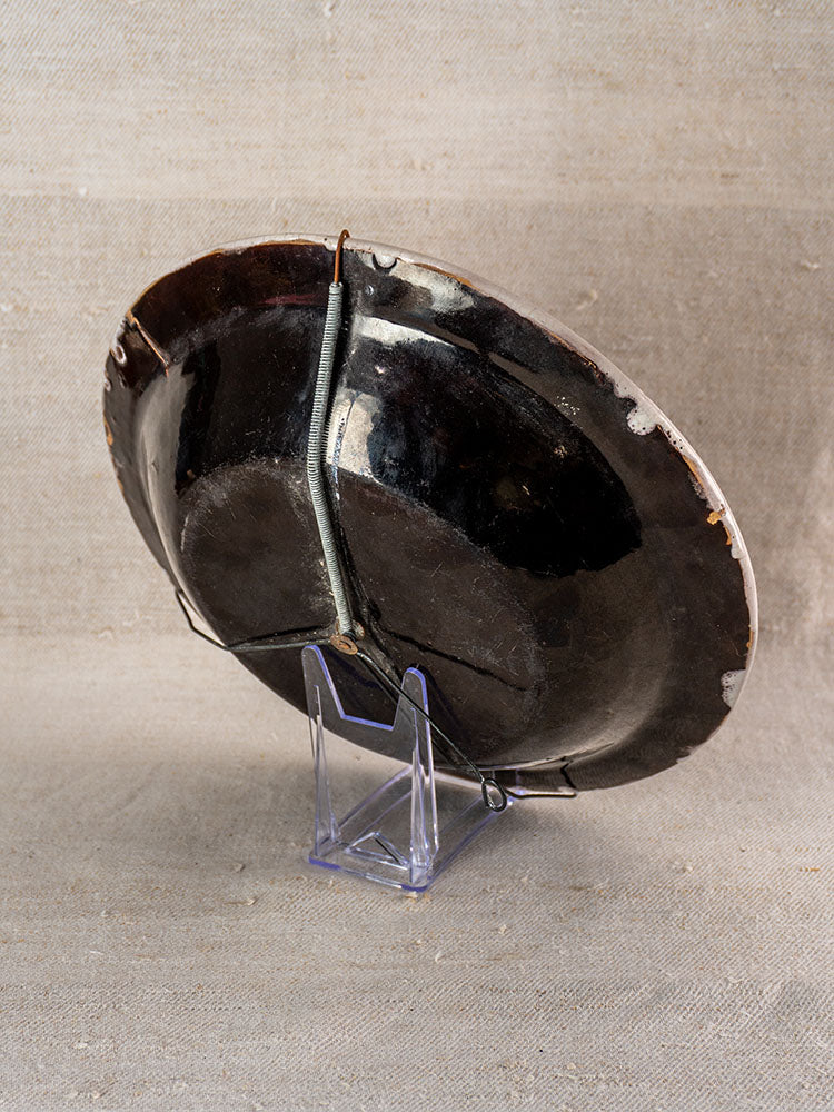 Late 18th-century French Cul Noir faience charger with Panier Fleuri motif, staple-repaired, on clear stand and beige fabric.