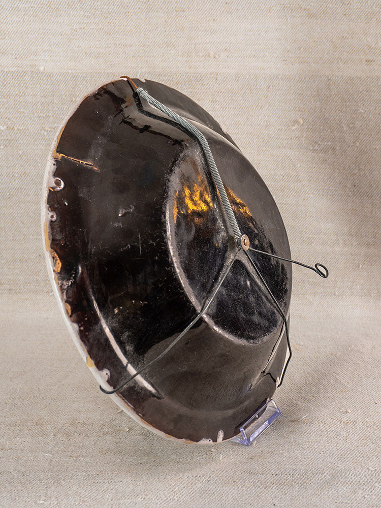 Antique French Cul Noir faience charger with Panier Fleuri, metal-staple repaired cracks, on clear stand with fabric backdrop.