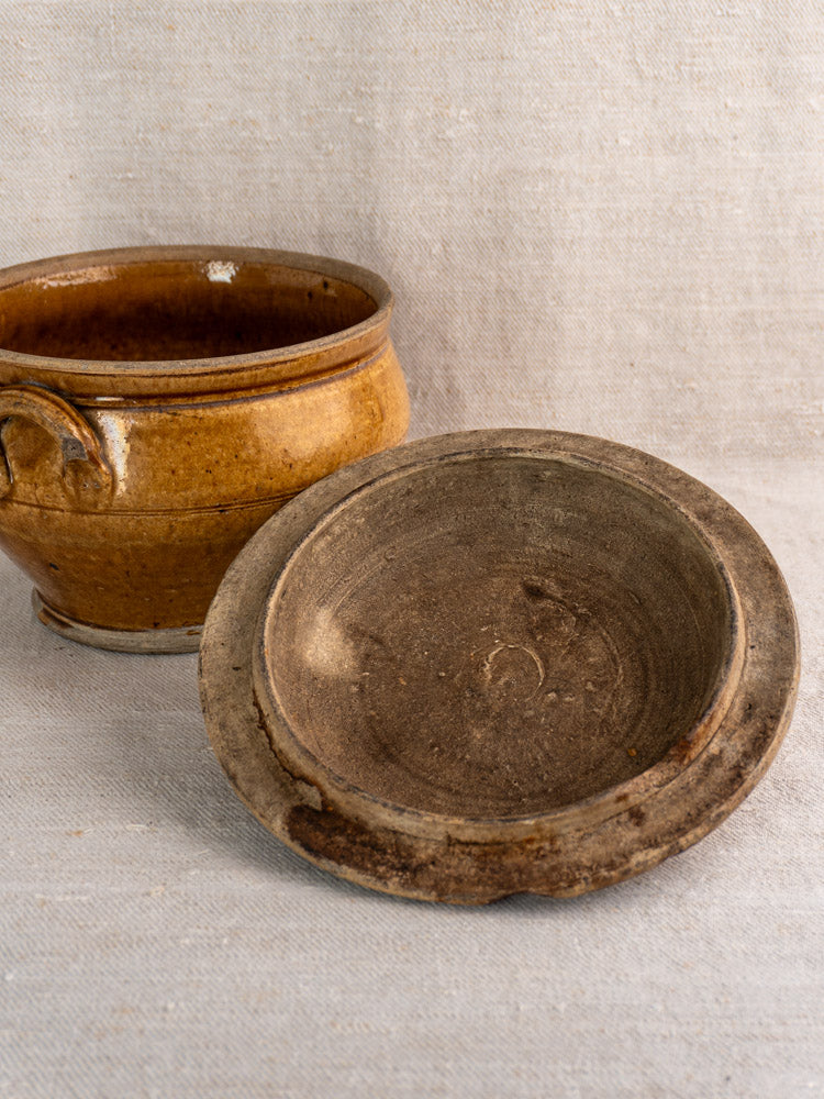 19th-century French grès lidded stoneware pot with honey glaze and handle on beige fabric background.