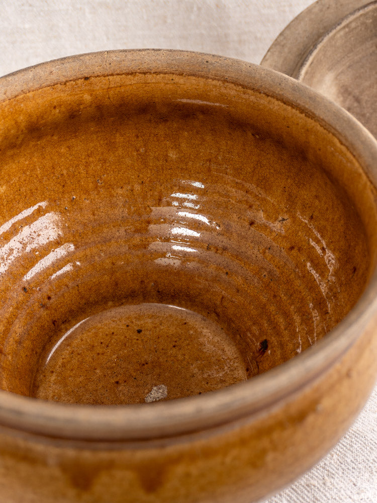 Brown ceramic bowl with honey-glazed interior and circular ridges, beside antique French stoneware pot.