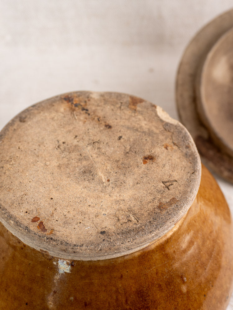 Antique French lidded stoneware pot with honey glaze, unglazed base; similar pot in background.