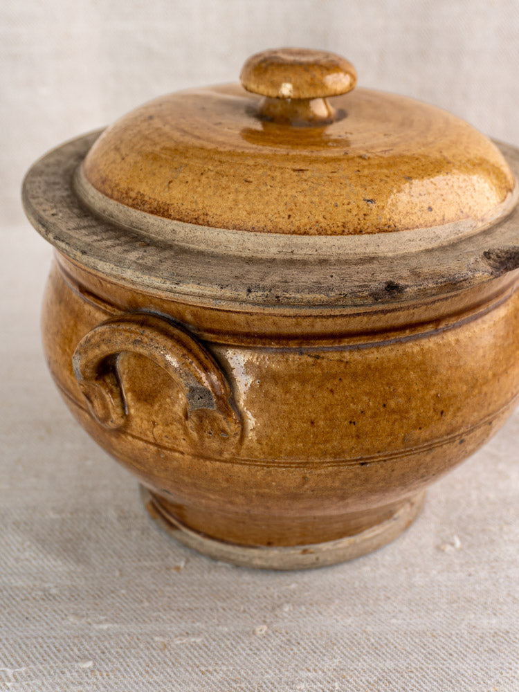 19th-century French lidded stoneware pot in honey-glazed grès with small handle on fabric surface.