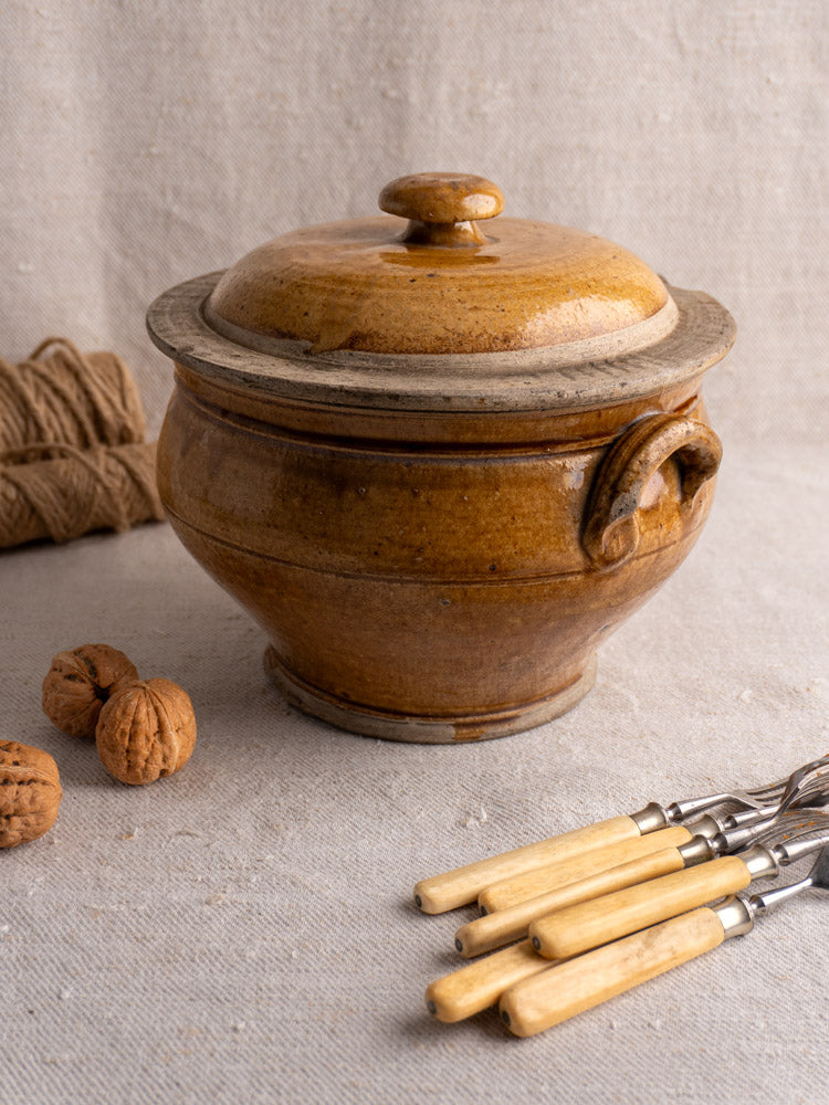 Antique French lidded stoneware pot in honey-glazed grès, shown with walnuts and vintage flatware.