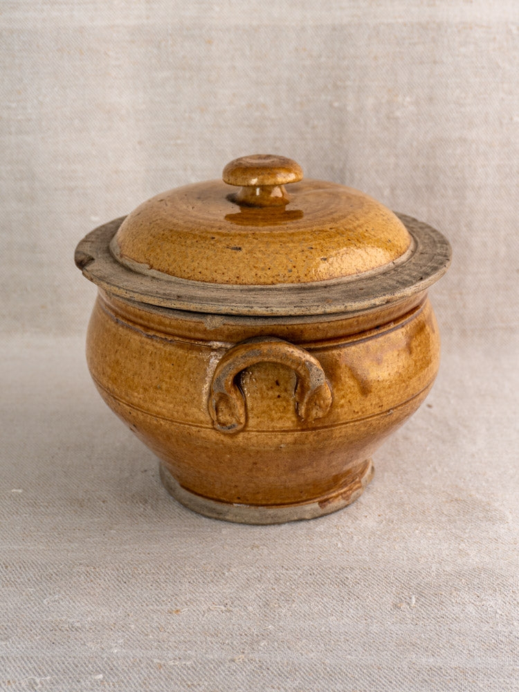 Antique French lidded stoneware pot in honey-glazed grès with two handles on textured fabric.