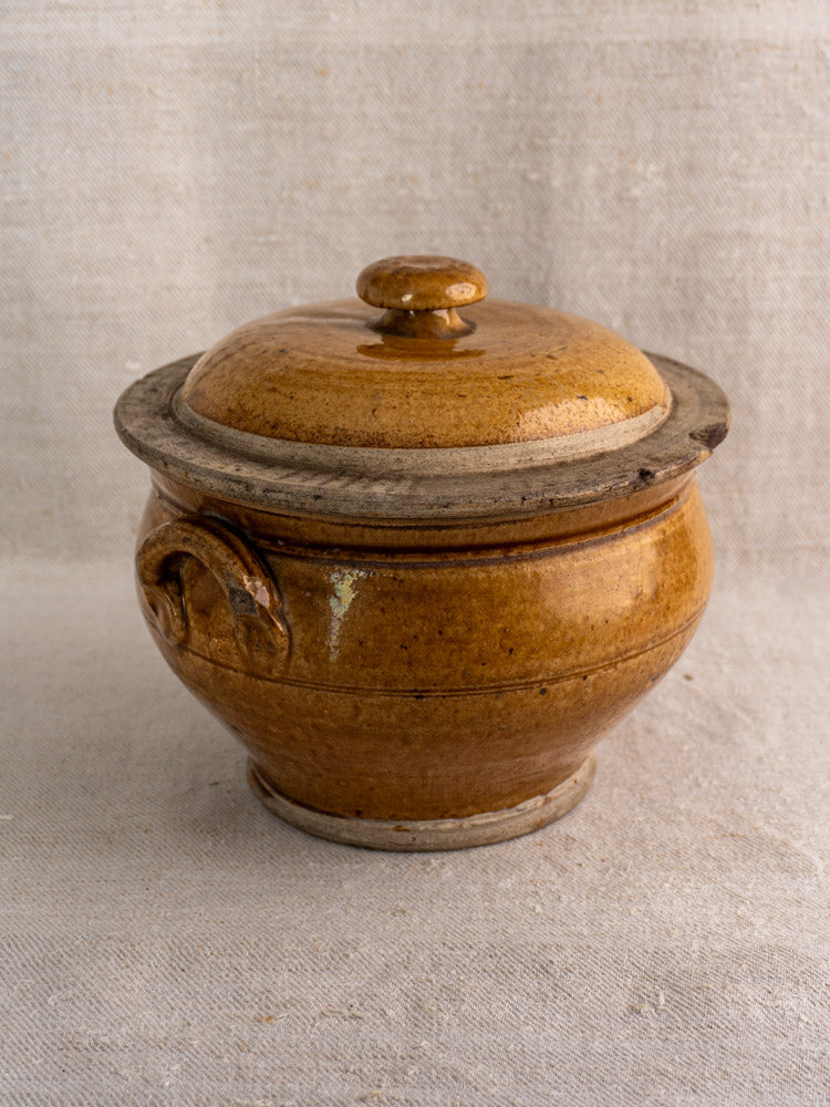 Antique French lidded stoneware pot with handle, 19th-century honey-glazed grès on light fabric.