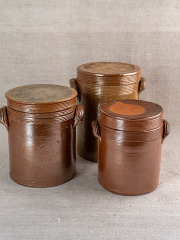 Set of three antique French stoneware confit pots with handles, varying sizes, displayed on neutral fabric.