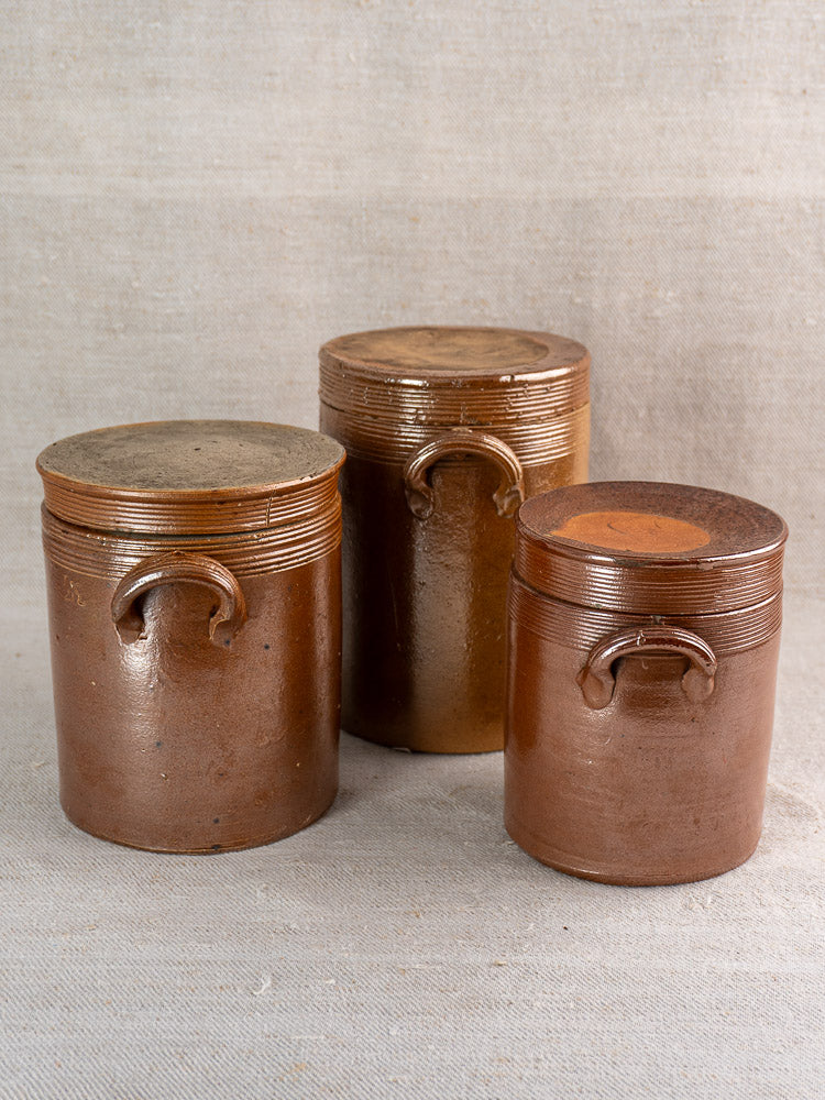 Set of three antique French stoneware confit pots with lids and handles, classic Provence farmhouse decor.