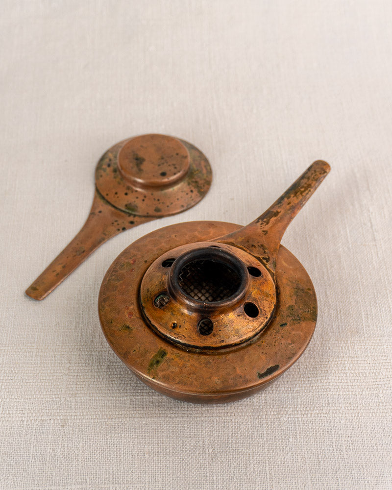Pair of antique bronze oil lamps with long handles and perforated lids, showing weathered patina on light textured surface.