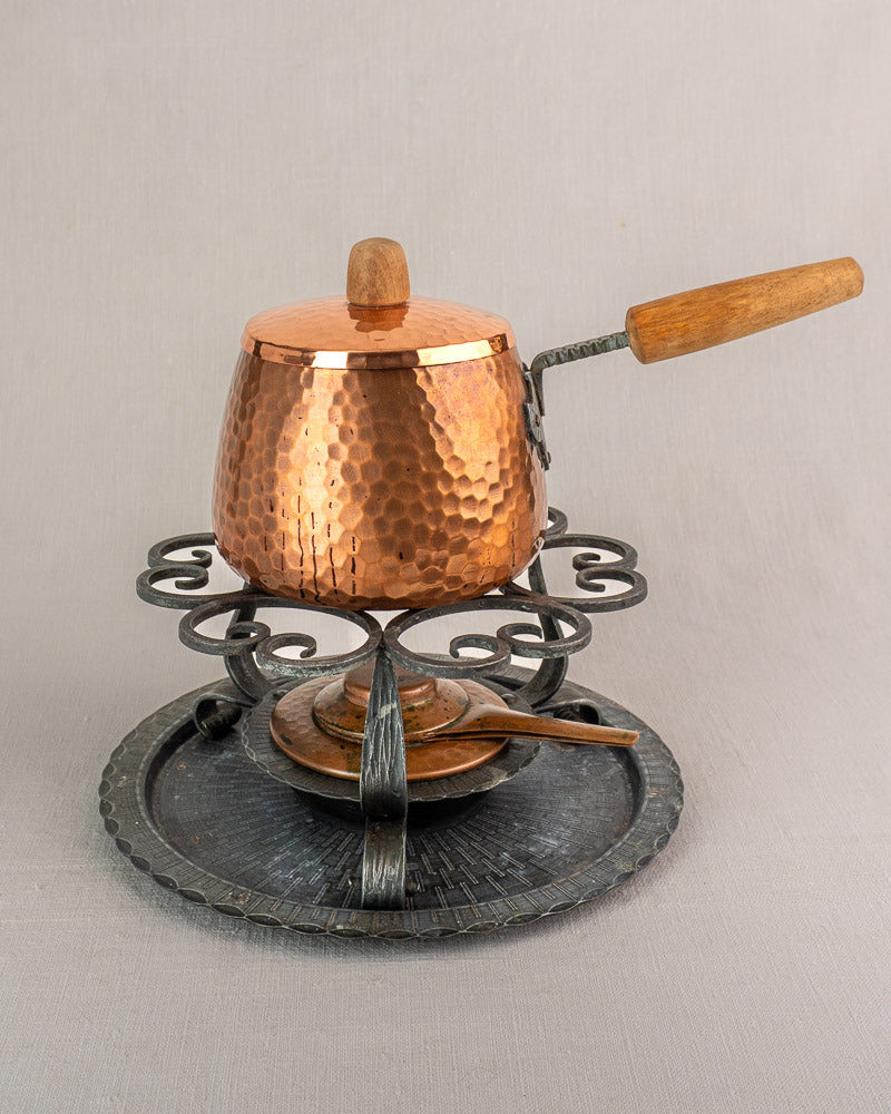 Antique French hammered copper fondue set with wooden handle, lid, ornate iron stand, burner, and matching fork.