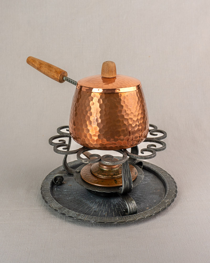 Antique French hammered copper fondue set with wooden handle, lid, iron warmer stand, and round tray.