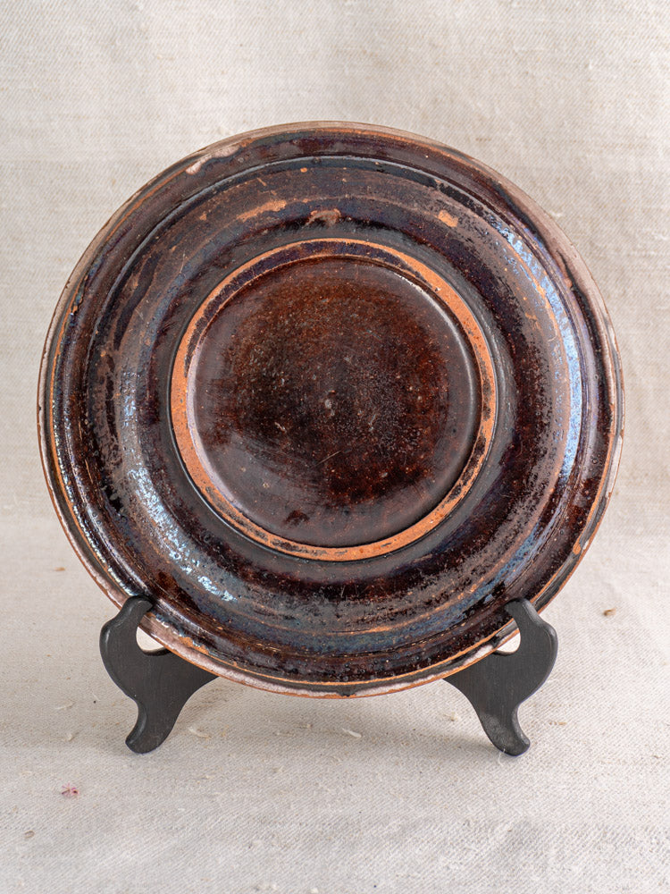 Antique French faience plate with hand-painted rooster, late 19th century, on black metal stand, neutral fabric backdrop.