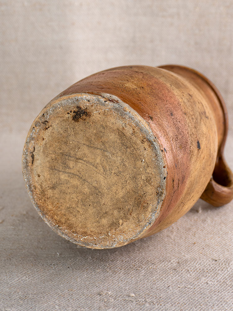 Antique French stoneware pitcher base with unglazed, textured bottom and minor imperfections on beige fabric.