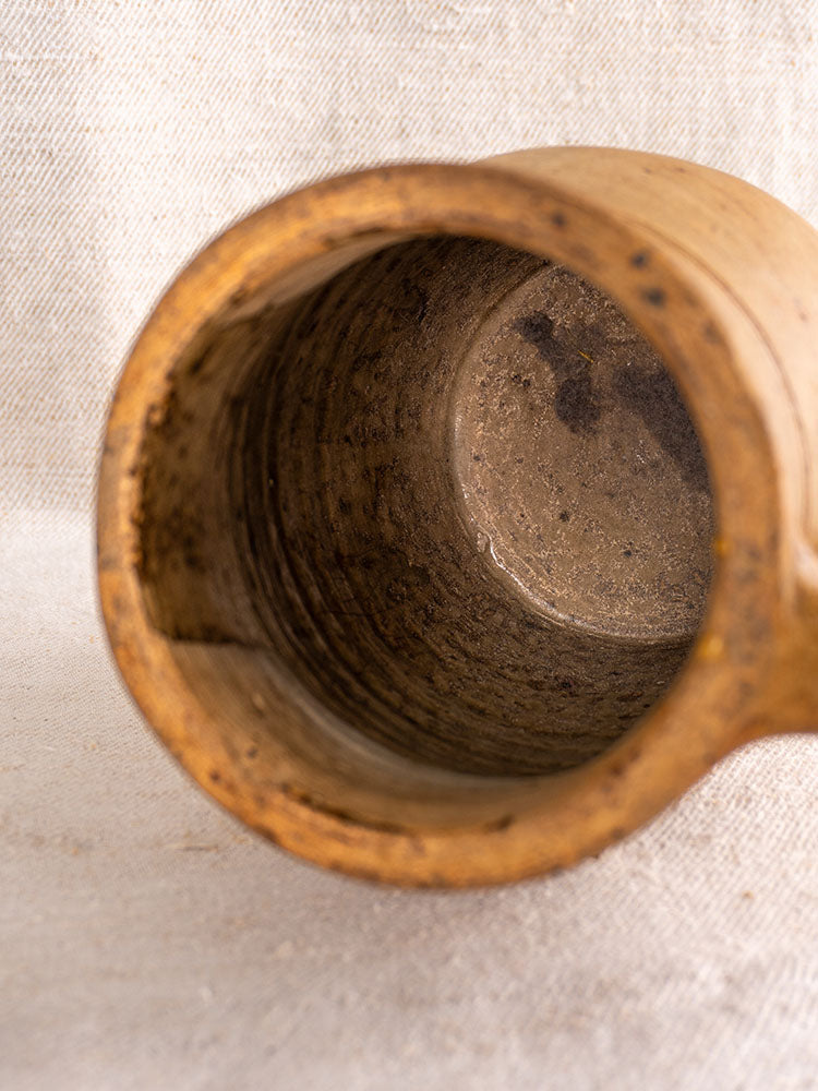 Antique French stoneware pitcher interior with rustic, earthy salt-glazed finish on textured light fabric surface.