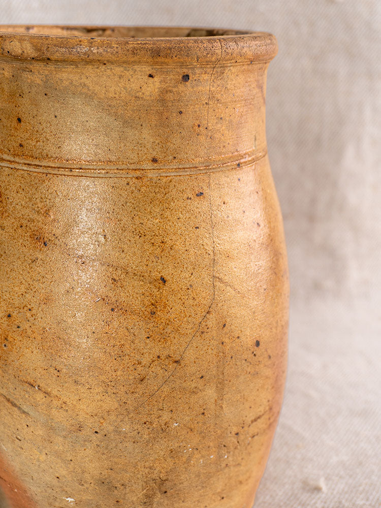 Early 19th-century French stoneware pitcher, salt-glazed grès in rustic brown with speckles, on textured light fabric background.