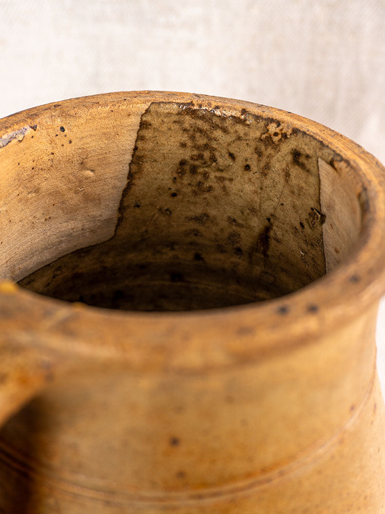 Rim and interior detail of early 19th century French salt-glazed stoneware pitcher with rustic wear and chipped edge on fabric.