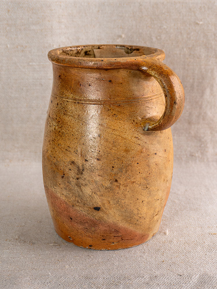 Rustic brown clay mug with natural imperfections, inspired by antique French salt-glazed stoneware, on beige fabric background.