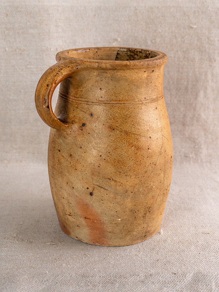 Antique French stoneware pitcher, early 19th century, salt-glazed grès with rustic brown finish on textured beige fabric.