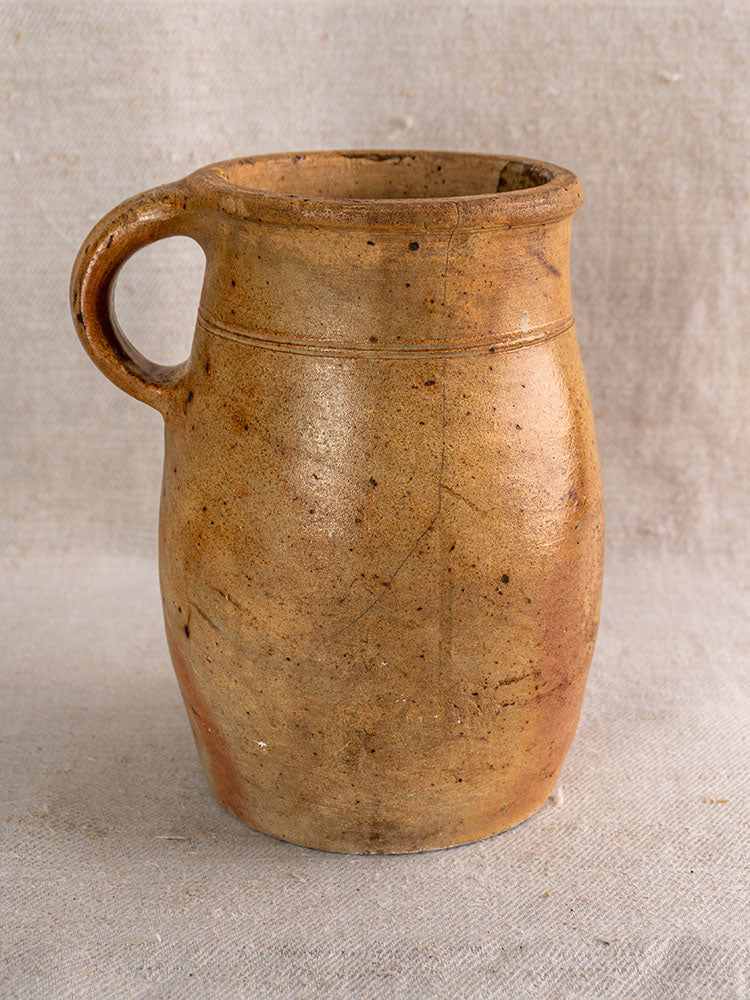 Early 19th-century French stoneware pitcher with salt-glazed grès, light brown finish, and rustic patina on neutral fabric.