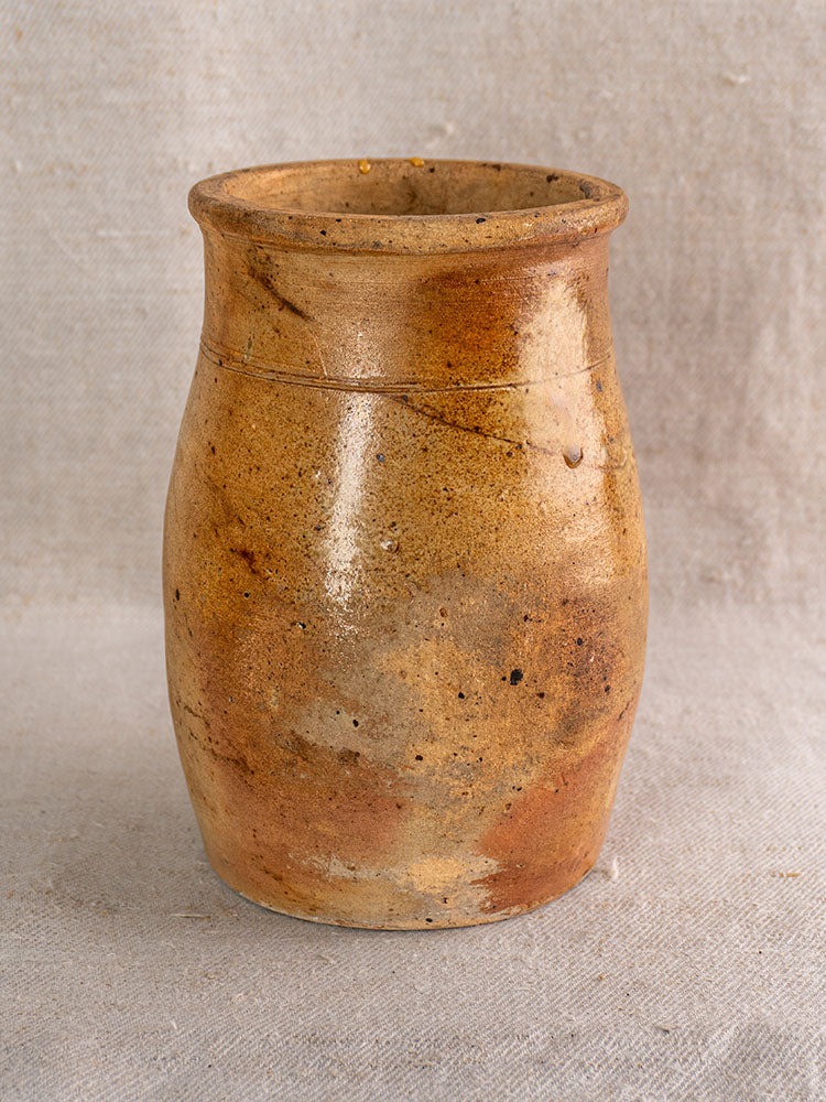 Antique French salt glazed stoneware pitcher with rustic brown body, flared rim, textured surface on neutral fabric background.