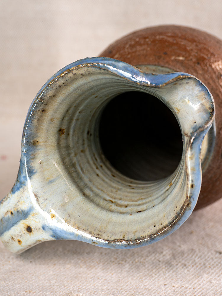 Antique French stoneware pitcher from La Borne with wide spout and blue ash celadon glaze on light textured fabric.