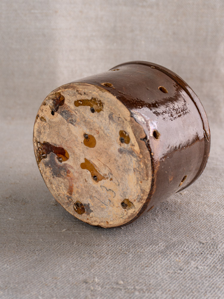 Pair of 19th century French ceramic cheese strainers with unglazed bottoms and drainage holes on beige fabric background.