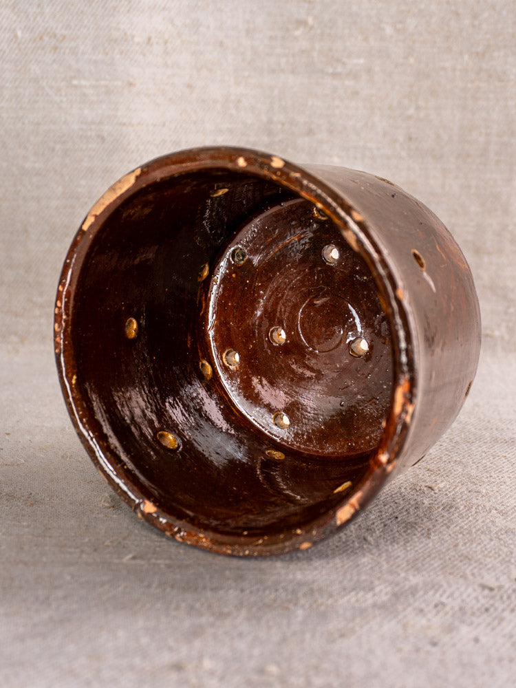 Pair of 19th century French glazed ceramic cheese strainers with drainage holes, shown on neutral textured fabric.