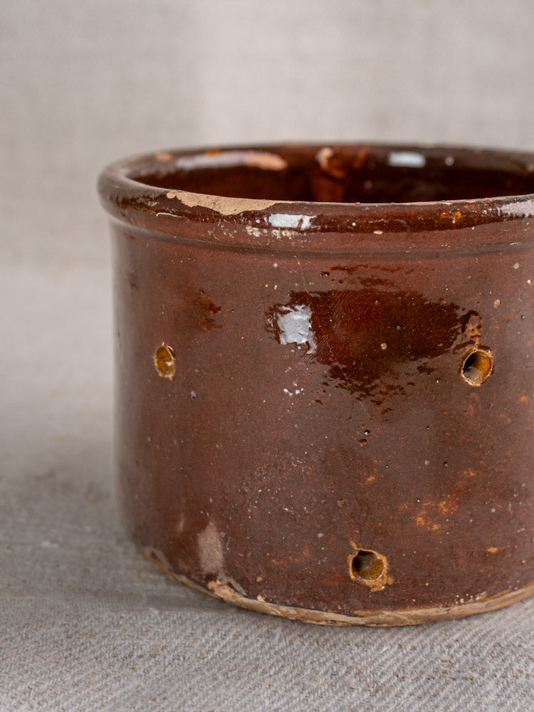 Pair of 19th century French ceramic cheese strainers with glossy brown glaze and small drainage holes on neutral textured fabric.