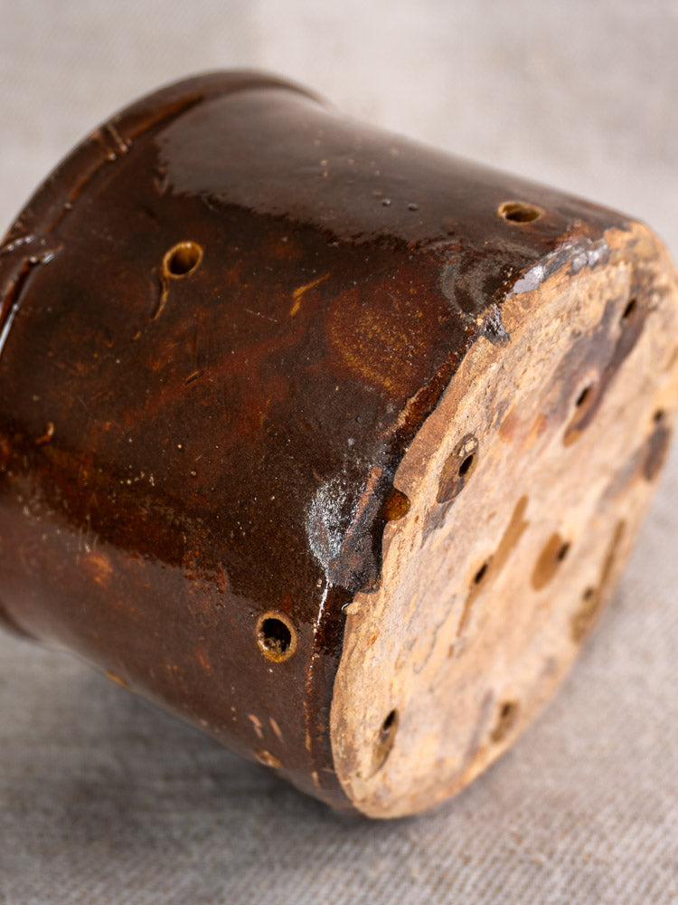 Pair of 19th-century French ceramic cheese strainers, brown glazed cylinders with perforations and unglazed bases on neutral fabric.