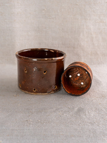 Pair of 19th-century French ceramic cheese strainers, round and brown with lids, on light textured fabric.