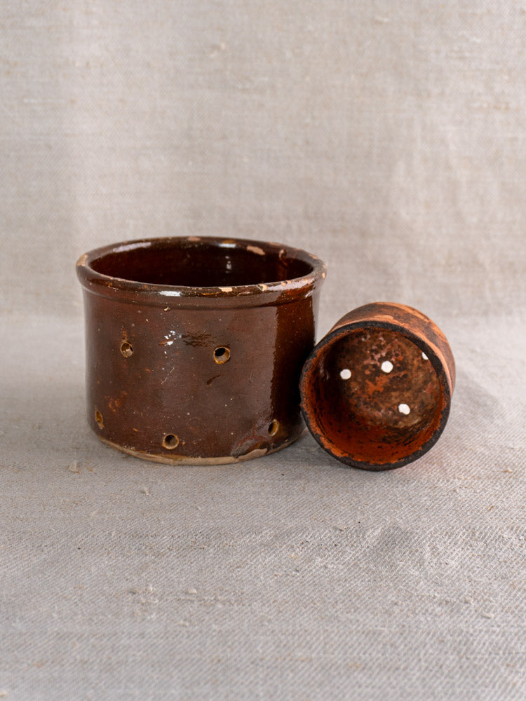 Pair of 19th-century French ceramic cheese strainers, round and brown with lids, on light textured fabric.