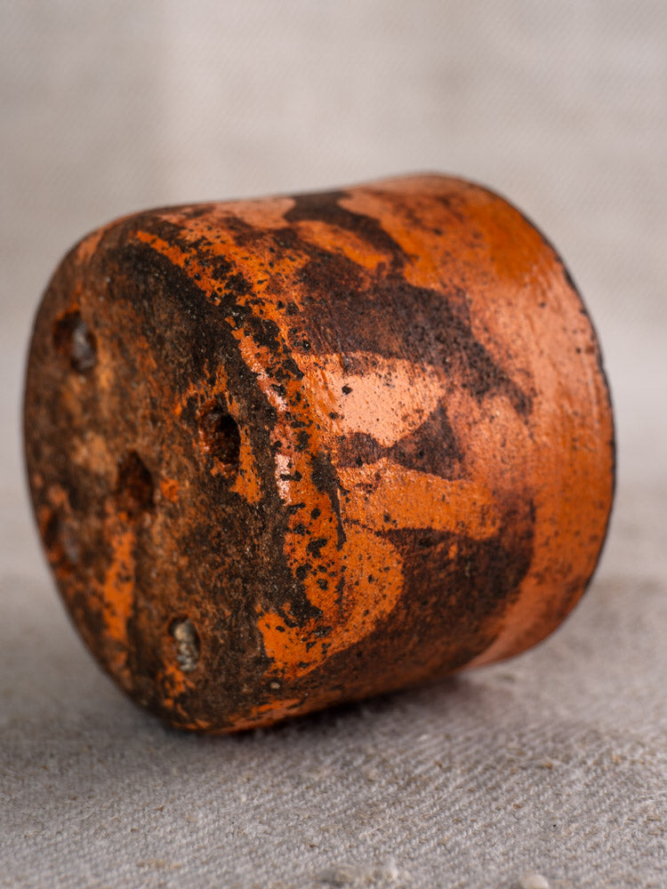 Pair of 19th century French ceramic cheese strainers with orange-black patina, three holes, on textured fabric background.