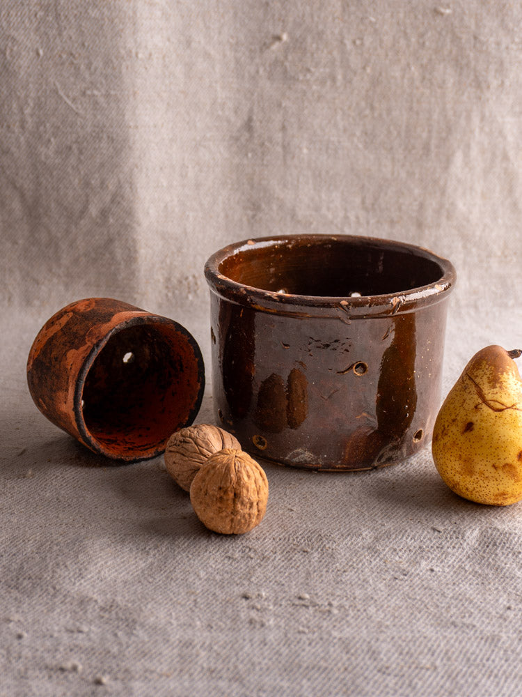 Pair of 19th century French ceramic cheese strainers with walnuts and a yellow speckled pear on a grey surface.