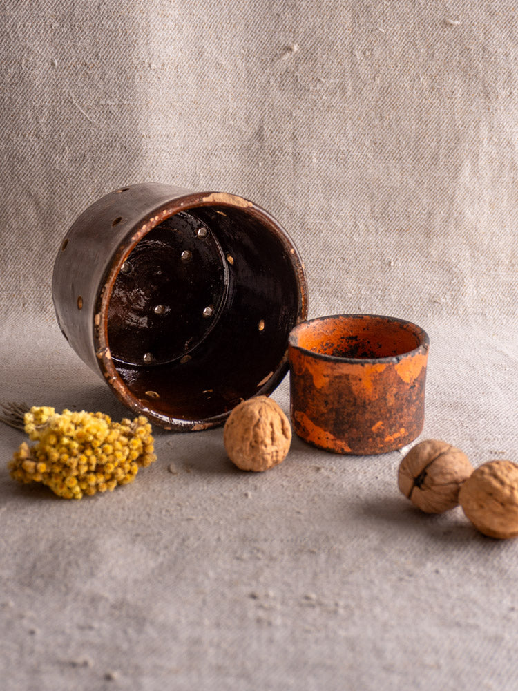 Pair of 19th-century French ceramic cheese strainers, round and brown with lids, on light textured fabric.