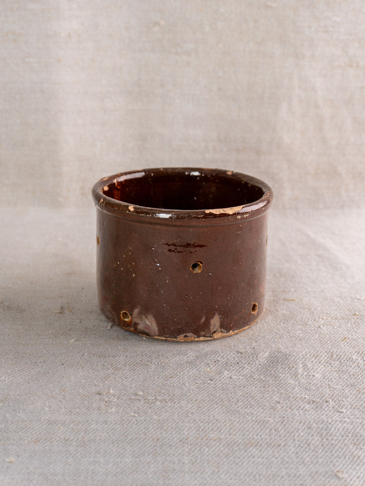 Pair of 19th century French ceramic cheese strainers, small, round, glossy brown, on textured beige fabric.