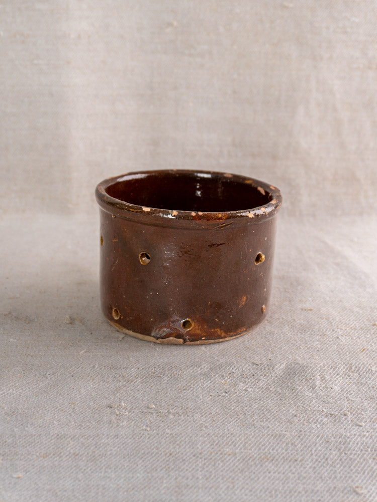 Pair of 19th-century French ceramic cheese strainers, small, dark brown, glossy, with side perforations on light textured fabric.