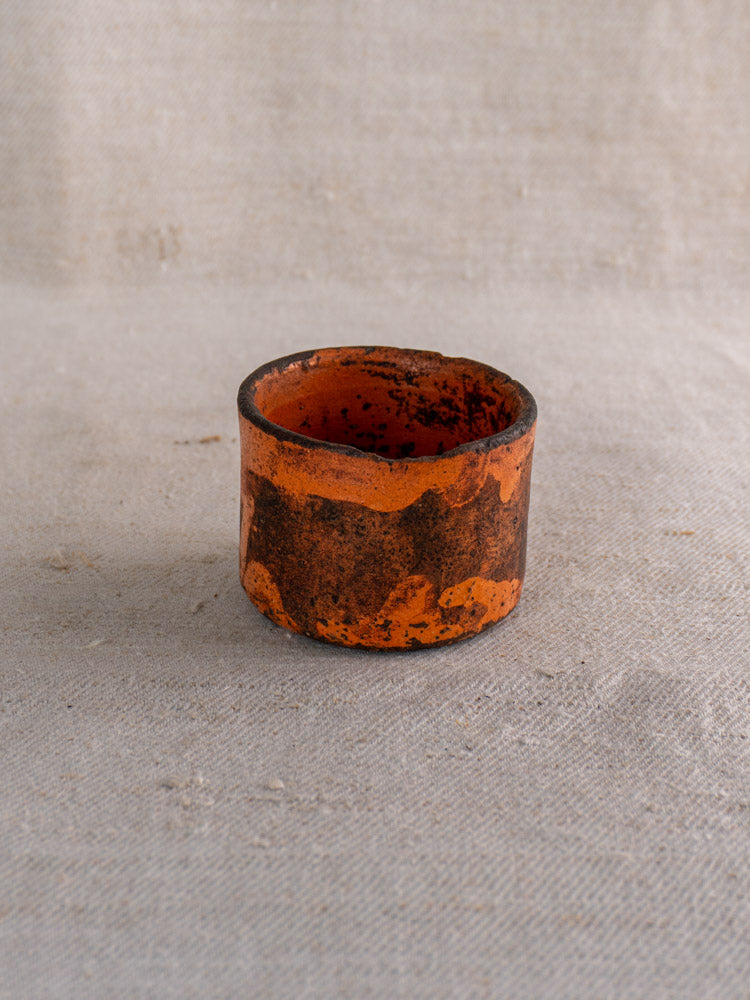 Pair of 19th century French ceramic cheese strainers with orange and black glaze on neutral fabric background.