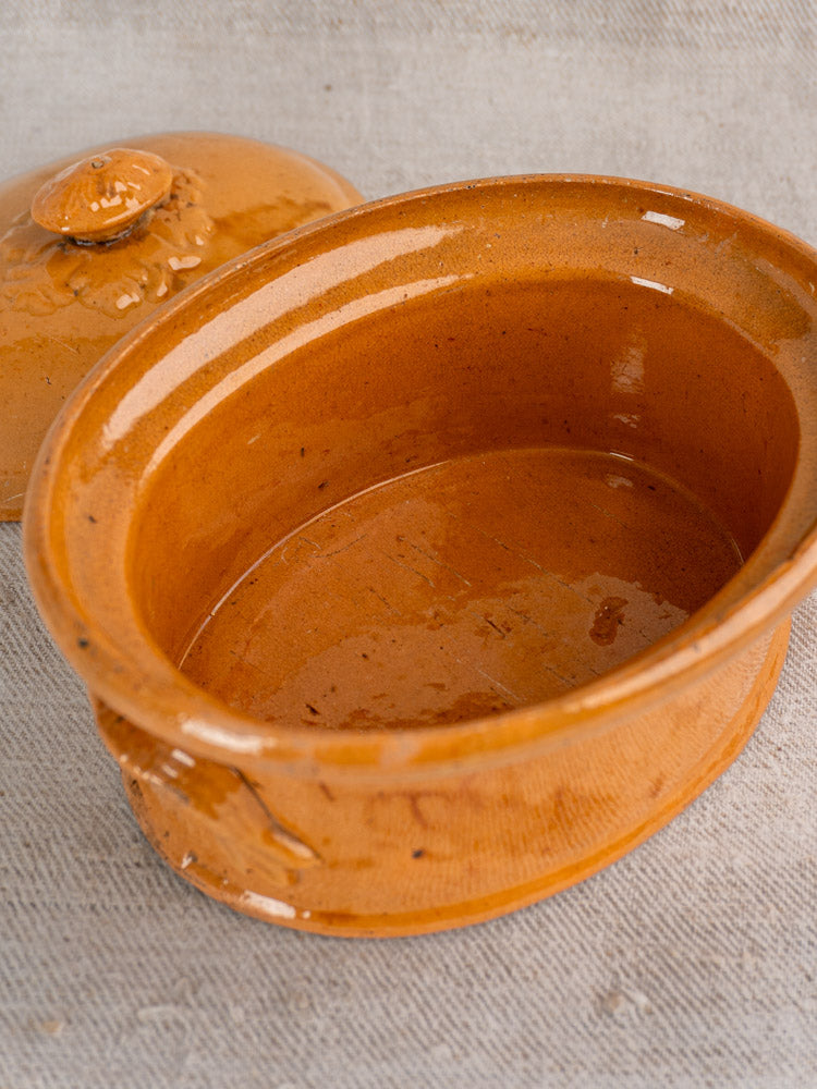 Antique French terrine in mustard ochre glaze with lid, slightly tilted to reveal glossy interior on light textured fabric.