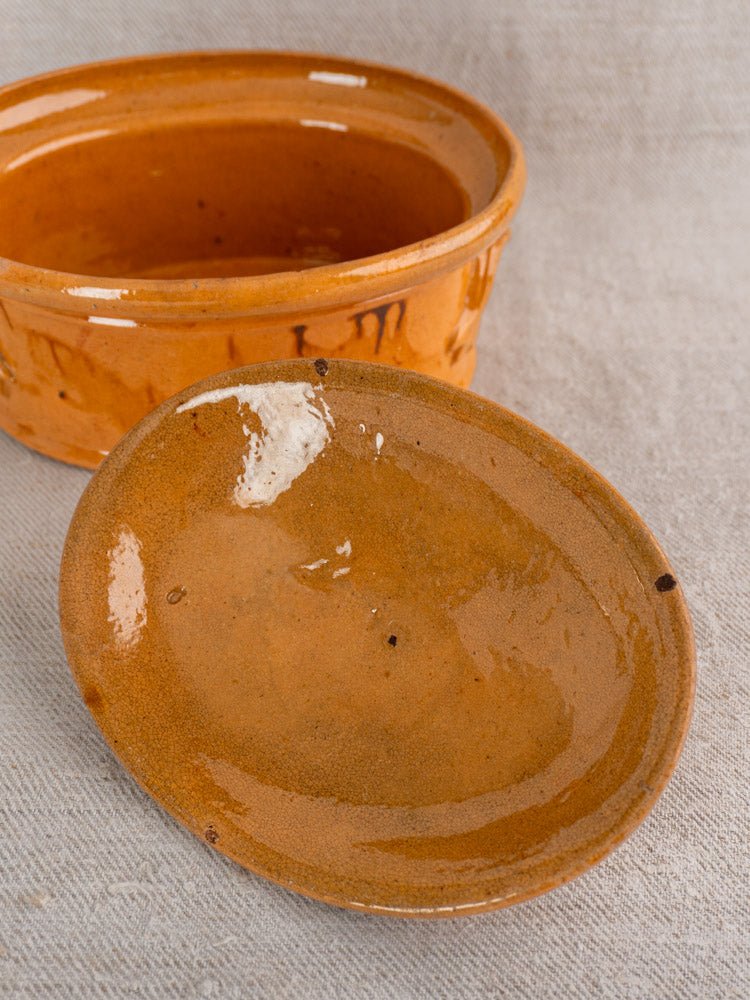 Antique French terrine with mustard ochre glaze, handmade Vendeuvre faience, displayed on neutral beige fabric.