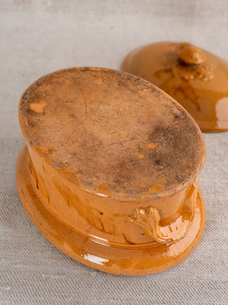 Antique French terrine with mustard ochre glaze, upside down on textured fabric; matching glossy lid beside it.