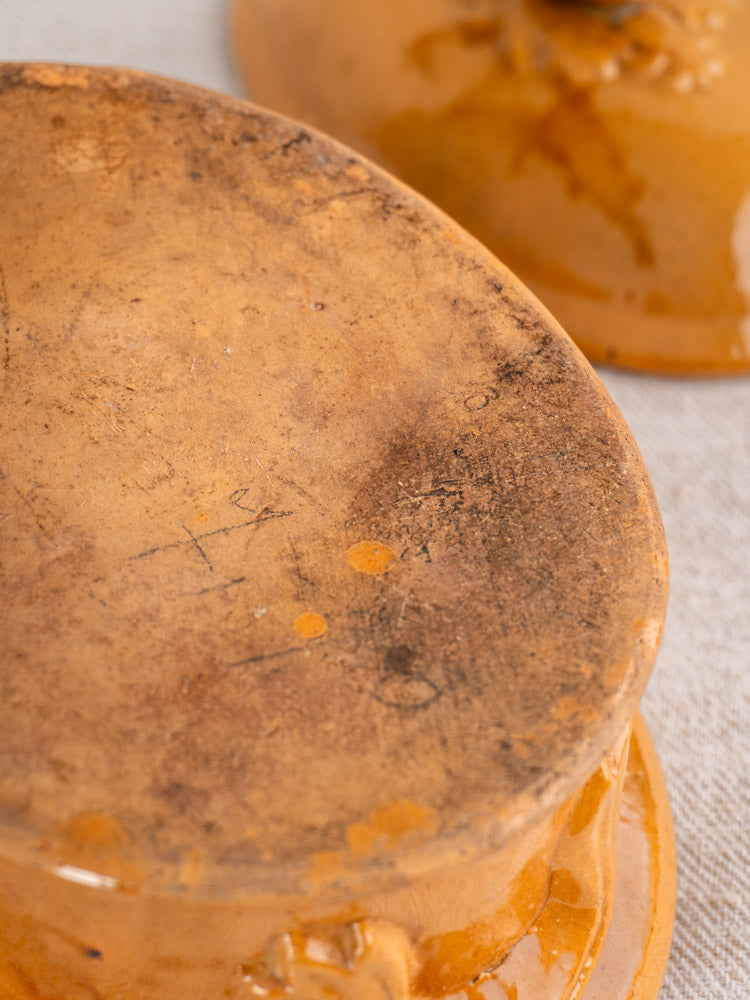 Worn, textured base of antique French terrine in mustard ochre glaze with matching dish partially visible in background.