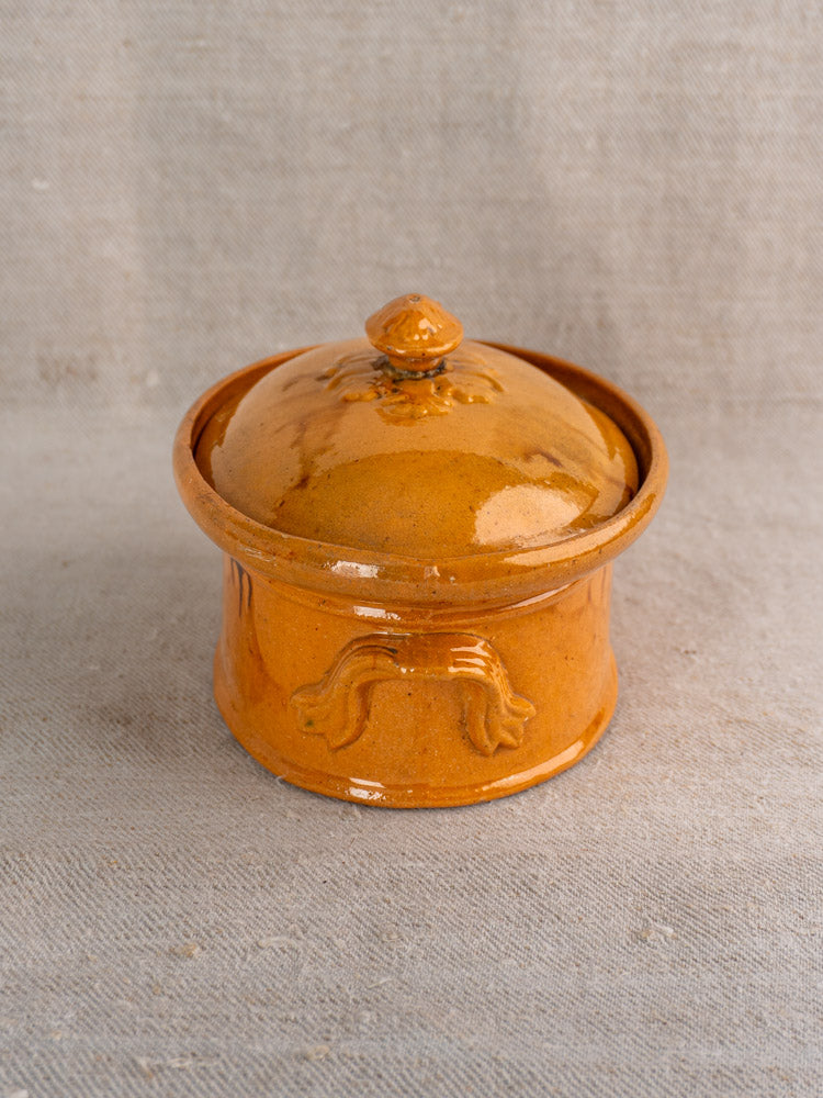 Antique French terrine with lid and decorative handles in mustard ochre glaze on beige textured fabric background.